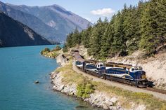 a train traveling along the side of a mountain next to a body of blue water