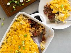 a casserole dish with meat, cheese and green onions in it next to a serving spoon