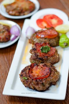 three hamburger patties with tomatoes and onions on a white plate, ready to be eaten