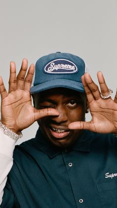 a man in a blue shirt and hat holding his hands up to the side while wearing a supreme hat