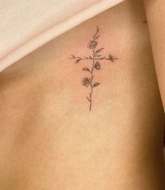 a small cross tattoo on the back of a woman's left ribcage