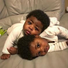 two small children laying on top of a couch next to each other, looking at the camera