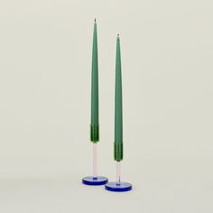 two green candles sitting next to each other on top of blue bases with pink tops