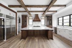 a large kitchen with wooden beams and white counter tops, hardwood flooring, and stainless steel appliances