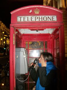 a woman is talking on the phone in a red telephone booth