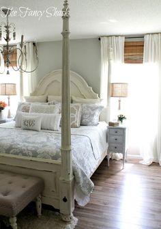 a white bed sitting in a bedroom on top of a hard wood floor next to a window