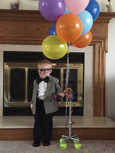 a young boy wearing glasses and a bow tie standing next to a bunch of balloons