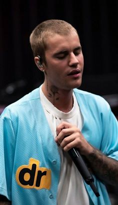 a man with tattoos on his arm holding a microphone and wearing a blue baseball jersey