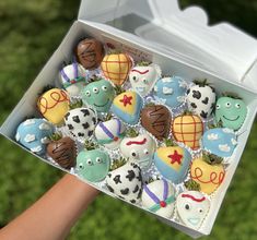 a box filled with lots of decorated cupcakes on top of a green field