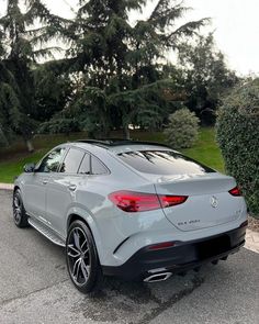 the rear end of a silver mercedes suv parked in front of some bushes and trees