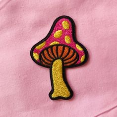 a pink shirt with a yellow and red mushroom patch on the front, embroidered onto it