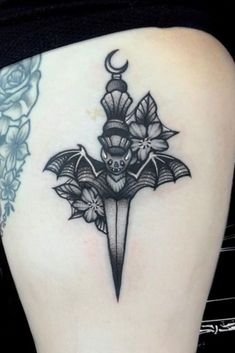 a woman's thigh with a bat and flower tattoo on her lower back leg