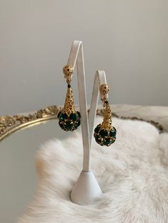 These are vintage mid-century clip on earrings. They are in a gold tone metal that is bright and shows no signs of wear or tarnish. The base of the earrings have round shape emerald tone rhinestones that form a sphere. The earrings are in excellent condition.Measurements:Length: 2" | Width: .75"Unless otherwise stated all vintage items are used and may have minor to moderate wear or discoloration considering the age of the item. Most items have been hand washed, spot cleaned, or professionally d Clip-on Drop Earrings For Bridal Evening, Formal Jeweled Drop Clip-on Earrings, Evening Metal Clip-on Chandelier Earrings, Vintage Gold Earrings For Evening, Clip-on Metal Chandelier Earrings For Evening, Gold Costume Jewelry Earrings For Wedding, Gold Drop Clip-on Earrings For Party, Gold Drop Clip-on Earrings For Evening, Vintage Gold Bridal Earrings