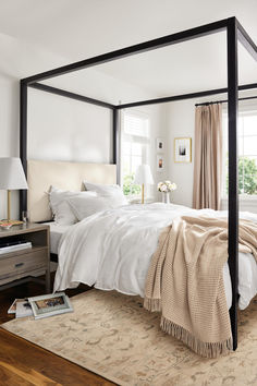 a four poster bed in a bedroom with white walls and wood flooring, along with an area rug on the floor