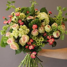 a woman holding a bouquet of flowers in her hand with green foliage and pink roses