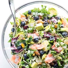 a salad in a glass bowl with silver spoons