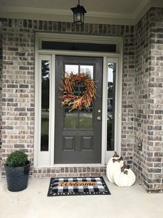 a front door with a wreath and two pumpkins