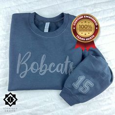 Get ready to show your school spirit with our new embossed/puff team name shirts, sweatshirts or hoodies! 🎉 Customize your look by choosing from different font styles to match your school's vibe. Perfect for cheering on your favorite teams in style! 🏆👕 Explore more fun and unique designs at https://www.etsy.com/shop/iconiquecrafts/ Our products are made to order and shipped from Texas, USA. Since our products are made to order, we do not accept returns or exchanges unless there is an error on Cheap Sports Fan Sweatshirt With Team Name, Cheap Sweatshirt With Team Name For Fans, Cheap Crew Sweatshirt With Team Name, Customizable College Fan Apparel Sweatshirt, School Crew Neck Sweatshirt With Team Name, College Varsity Sweatshirt With Name Print, Sporty Tops With Custom Logo For Game Day, Casual Customizable Sweatshirt For School, Custom Logo Crew Neck Tops For College