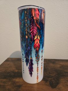 the colorful feathers are hanging from the handle of this tumbler cup, which is decorated with beads and chains