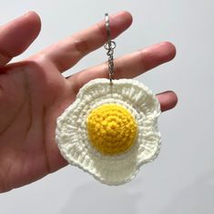 a hand holding a crocheted keychain with an egg in the middle