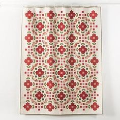 a red and white quilt hanging on the wall next to a curtain with flowers in it