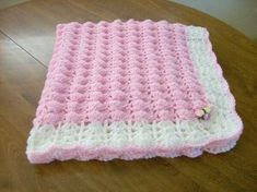 a pink and white crocheted blanket sitting on top of a wooden table