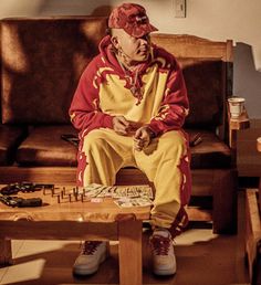 an old man sitting on a couch in front of a coffee table with several objects