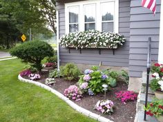 a house with flowers in the front yard and landscaping on the side walk, along with an american flag