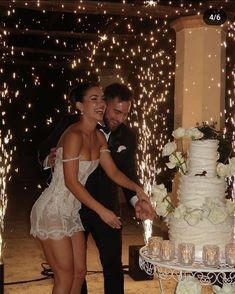 a newly married couple cutting their wedding cake with sparklers in the background at night