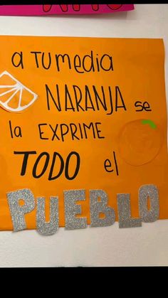 an orange sign hanging on the side of a wall with spanish words written below it