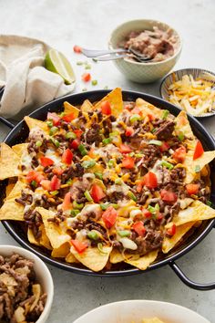 nachos with beef, cheese and tomatoes in a skillet on a table