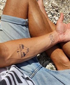 a man laying on the ground with his legs crossed and tattoos on his arm,