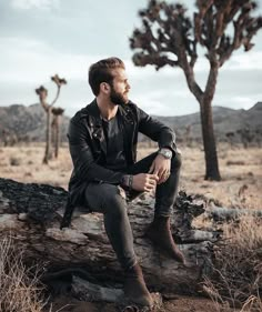 a man sitting on top of a log in the middle of a desert with trees