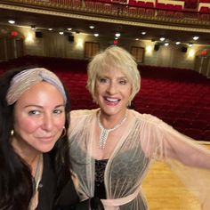 two women standing next to each other in front of an auditorium