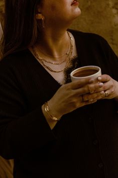 a woman holding a cup of coffee in her right hand and looking up into the sky