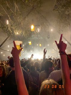 a large group of people at a concert with their hands in the air and lights above them