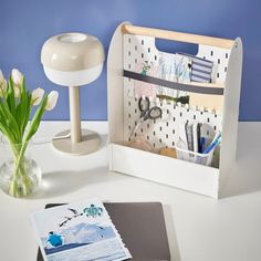 a white desk with a magazine holder and flowers in a vase