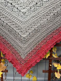 a crocheted shawl with red and grey colors on it sitting on a fence