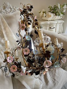 a chandelier with flowers and candles on it in front of a white bed