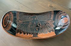 a black and brown bowl with an eagle design on the bottom, sitting on a wooden table