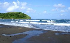 the beach has waves coming in to shore and green hills in the distance with blue sky