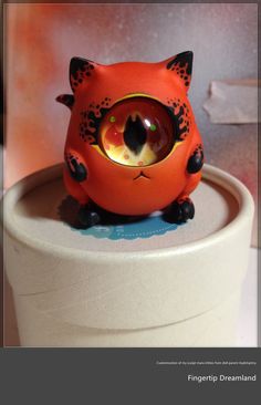 an orange cat figurine sitting on top of a round container with its eyes open