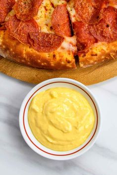 a pizza sitting on top of a wooden cutting board next to a bowl of sauce