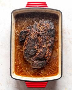 a meat dish in a red and white casserole on a white table top