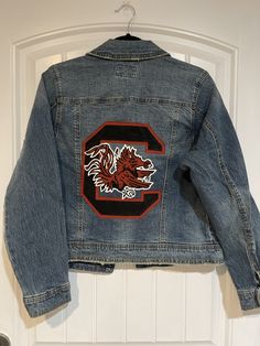 "Custom painted University of South Carolina Jacket.  *These are made to order. I currently do not have any completed of this design in stock. Please include the following information when purchasing: 1. Design idea (if different from photo) 2. Size of jacket  3. Date needed by (please note I have a 3-4 week processing time at the moment. if you need the jacket sooner please reach out to confirm with me that I can have it processed by the date you need it before purchasing) 4. Optional: any othe Custom Denim Jacket, Hand Painted Denim Jacket, Virginia Tech Hokies, Painted Denim Jacket, Coastal Carolina, University Of South Carolina, Custom Denim, Painted Jeans, Painted Denim