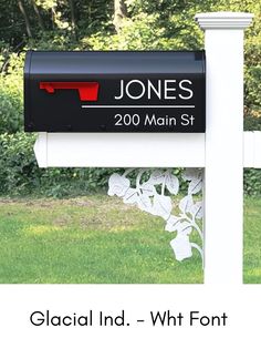 a mailbox in front of a white fence and some grass with trees behind it