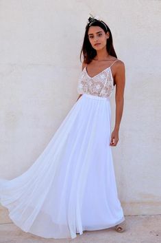 a woman wearing a white dress standing in front of a wall with her hand on her hip