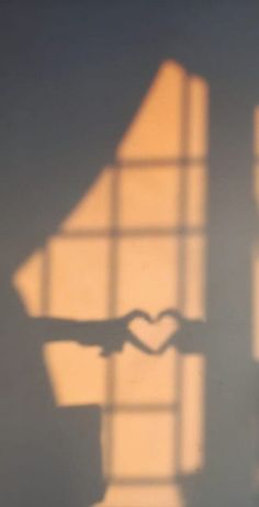 the shadow of a person's hand making a heart shape with their fingers in front of a window