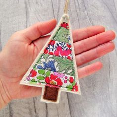 a hand holding a small christmas tree ornament on a string with flowers and leaves