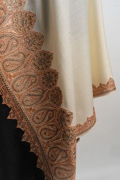 Step into a world of timeless elegance with our Ivory and Black Kashmiri Tilla Embroidered Merino Wool Shawl. This exquisite piece features delicate tilla embroidery in earthy tones, intricately embroidered along the borders. The harmonious blend of ivory and black creates a refined aesthetic that captures the essence Elegant Beige Embroidered Fabric For Festive Occasions, Elegant Beige Embroidered Fabric With Gold Details, Elegant Beige Embroidered Fabric, Elegant Beige Embroidered Fabric For Formal Occasion, Elegant Embroidered Fabric With Intricate Embroidery, Elegant Off-white Embroidered Fabric With Floral Design, Elegant Off-white Fabric With Floral Embroidery, Elegant Beige Floral Embroidered Fabric, Elegant Beige Resham Embroidered Fabric